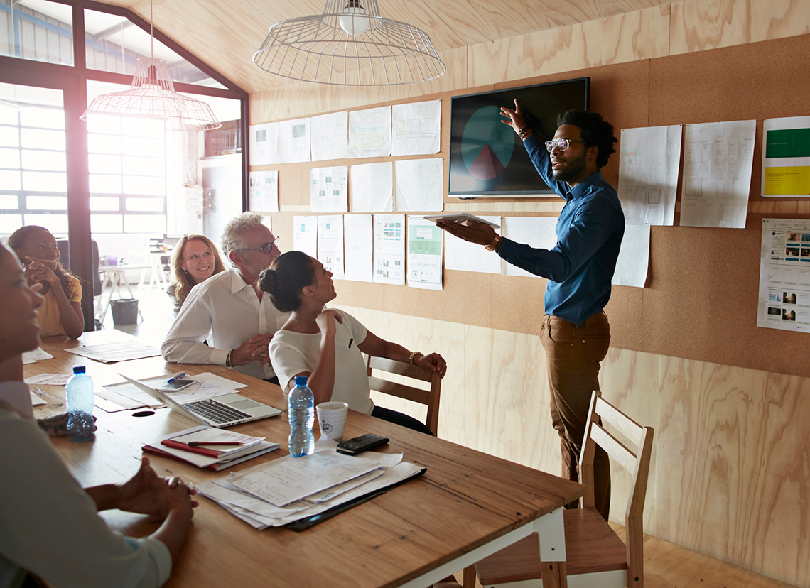 Person presenting in front of a few peers using a table and screen
