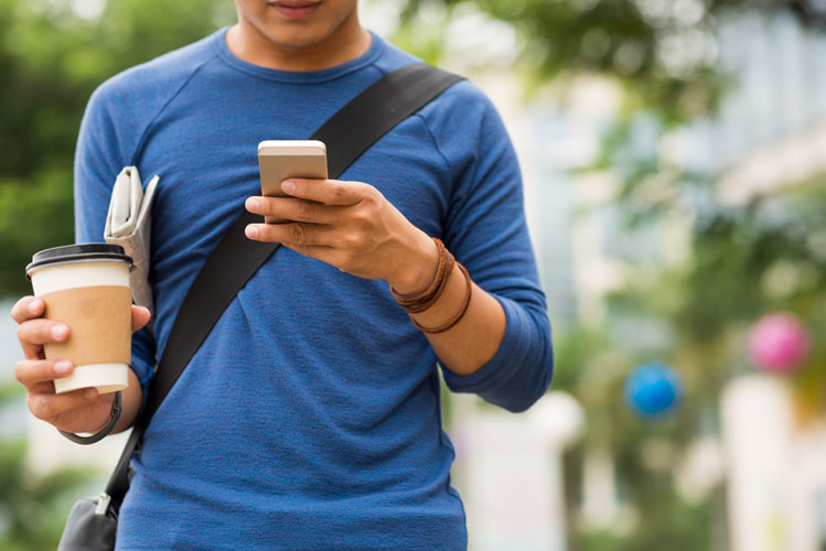 A person holding a cup of coffee in one hand and their smartphone in the other