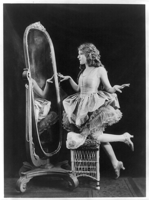 The Canadian actress Mary Pickford leaning on a chair and looking in a mirror.