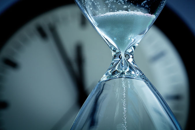 An hourglass with a clock behind it.