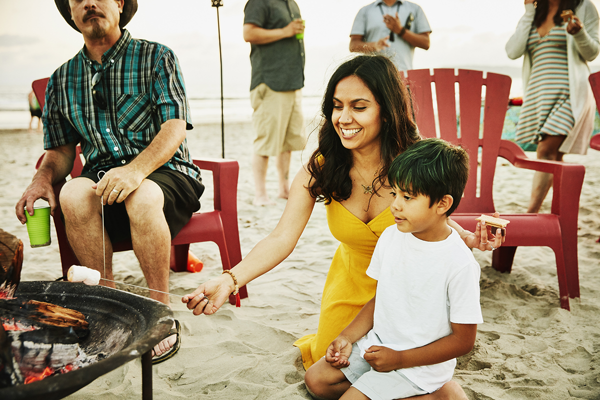 Person roasting marshmallows with a child on the beach