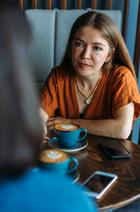 Two friends having coffee. One friend is leaning forward, listening, with a concerned expression