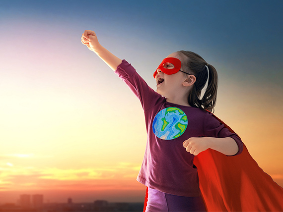 Child wearing a cape and a shirt with the Earth on it. Their hand is raised in a superhero pose.