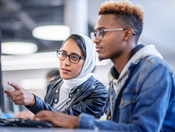Two people sitting at a computer. One person is pointing to the screen.