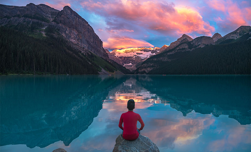 A person sits on a rock watching Lake Louise during the day.