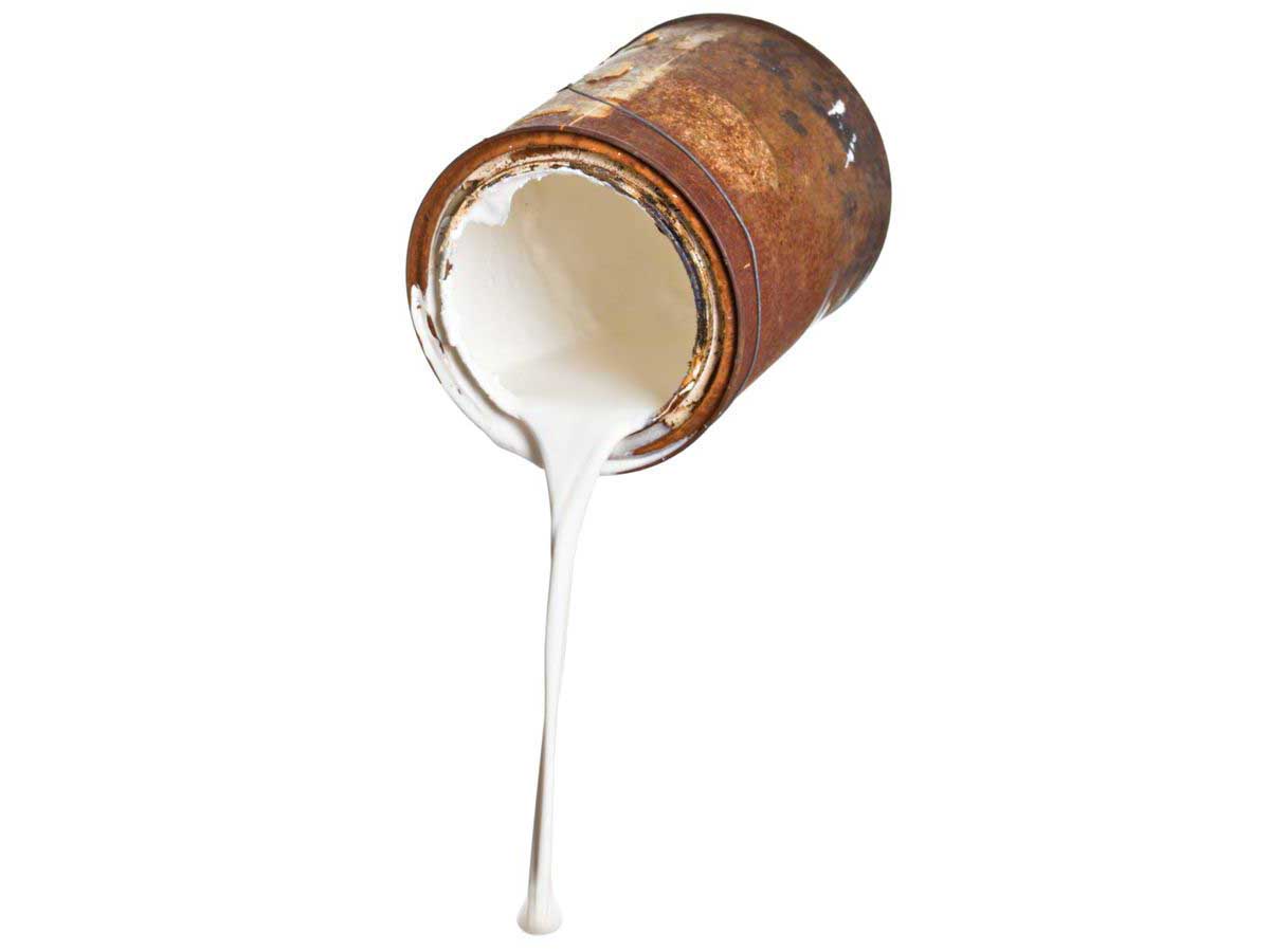 A close up of leaded white paint pouring out of an old rusty paint can